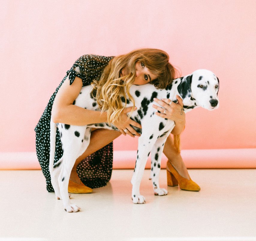 Kvinna kramar en dalmatin framför en rosa vägg.